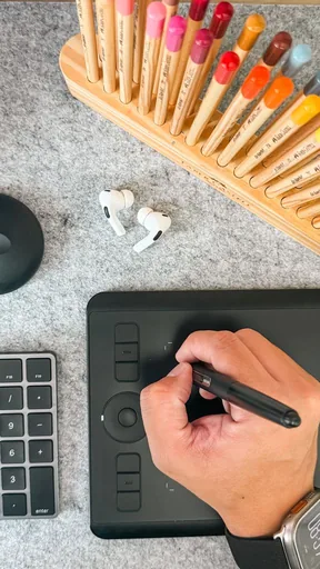 Overhead flat lay of a drawing tablet, stylus and colour pencils